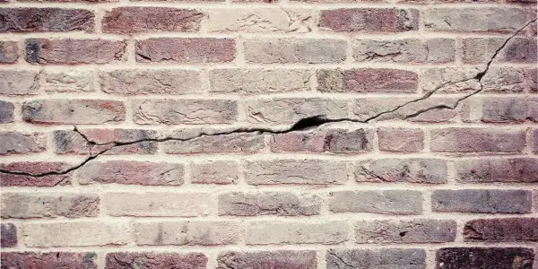 Een oude bakstenen muur met duidelijke scheuren die door de stenen lopen, getuigen van de tand des tijds.