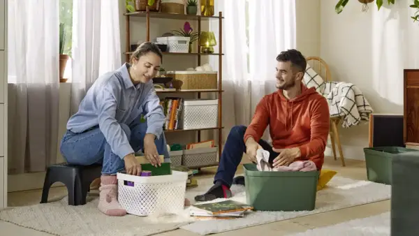 Een stel pakt spullen in, klaar voor hun reis van ontspullen in 52 weken. Ze sorteren boeken en kleding in opbergbakken.