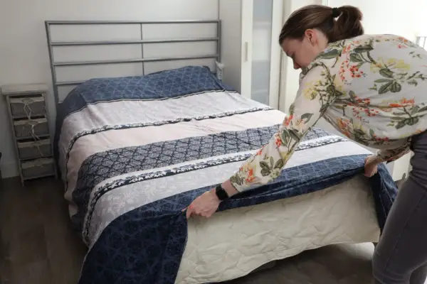Vrouw verschoont bed met een bloemenblouse. Een schone slaapomgeving is belangrijk, dus vraag je je af hoe vaak bed verschonen?