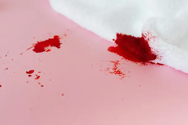 Bloedvlekken verwijderen? Oma weet raadt! Een witte doek absorbeert rode vlekken op roze ondergrond.
