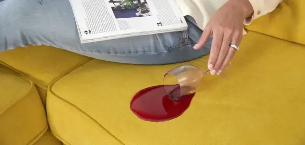 Een glas rode wijn is omgevallen op een gele bank. Hopelijk ruikt de bank straks weer lekker fris!