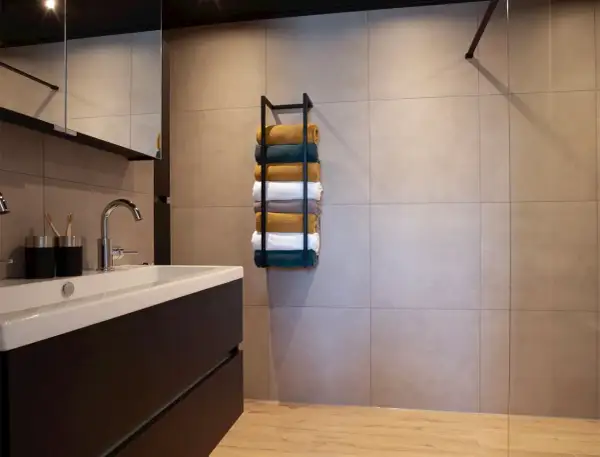 Netjes opgestapelde handdoeken in verschillende kleuren op een zwarte handdoekenrek in een moderne badkamer.