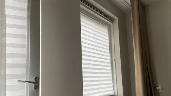 Wit plisségordijn als tijdelijke raambekleding tijdens een verbouwing. Een beige gordijn hangt ernaast.