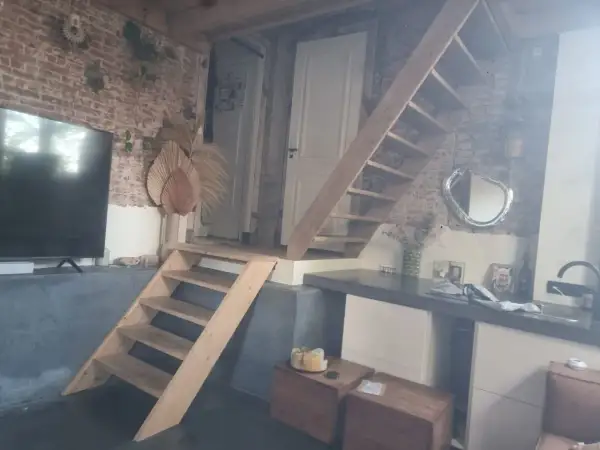 Een vide met een houten trap, bakstenen muur en een tv. Wat is een vide? Een open ruimte in een huis die meerdere verdiepingen verbindt.