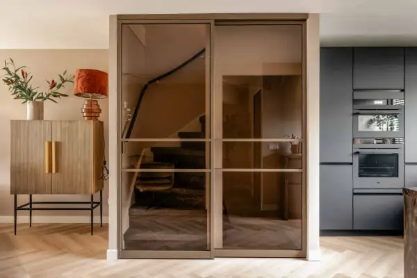 Moderne glazen schuifdeuren geven trapgat inspiratie. Een marmeren trap met donkere treden en een houten vloer.