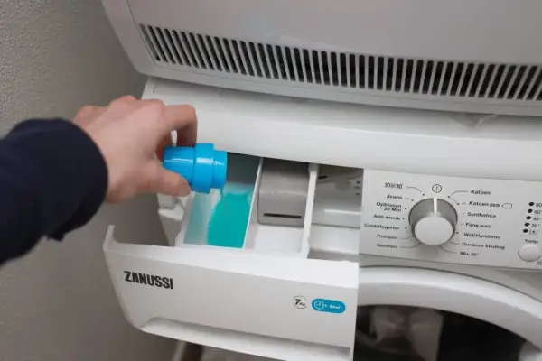 Hand giet blauw wasmiddel in het bakje van de wasmachine. Links of rechts, het bakje is duidelijk gemarkeerd.