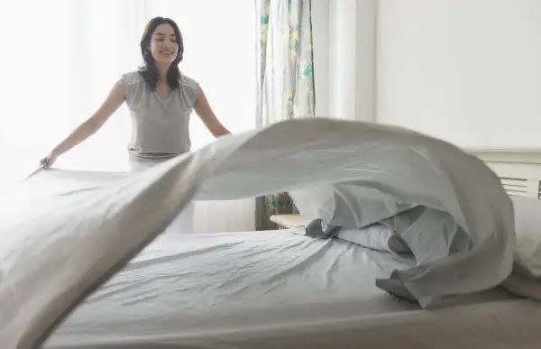 Vrouw verschoont beddengoed, zodat de slaapkamer lekker laat ruiken.